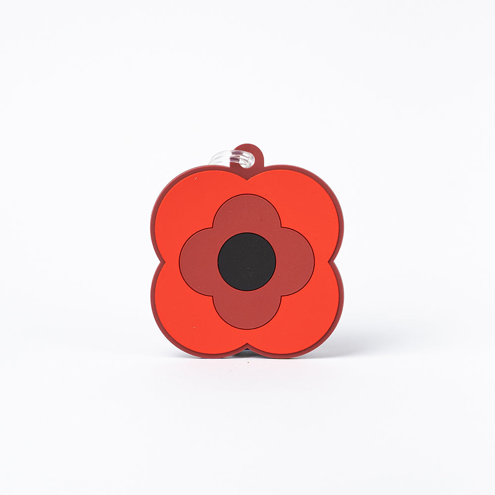 A luggage tag in the shape of a simplified poppy, in two shades of red with a black centre