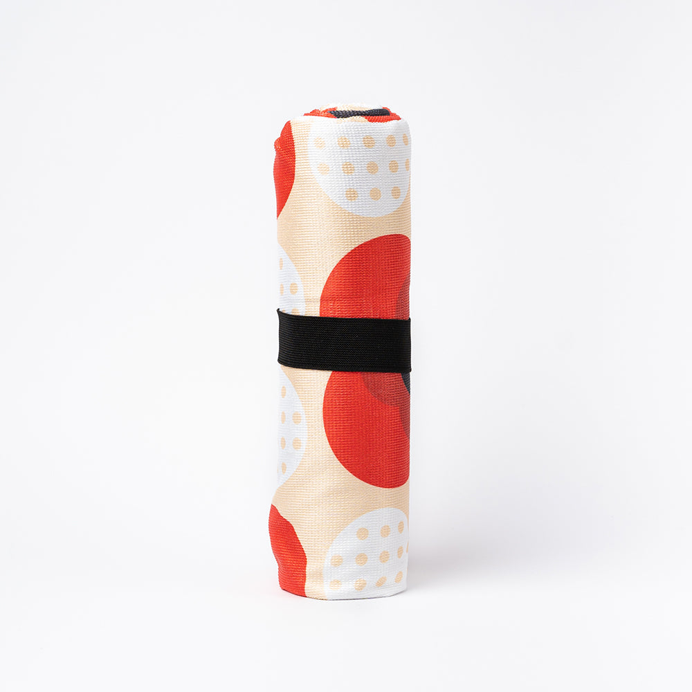 A beach towel featuring a stylised poppy design in red white and cream