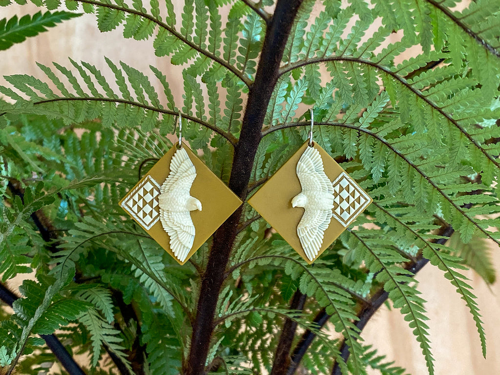 The earrings in a cream and gold colourway, hanging from a fern frond 